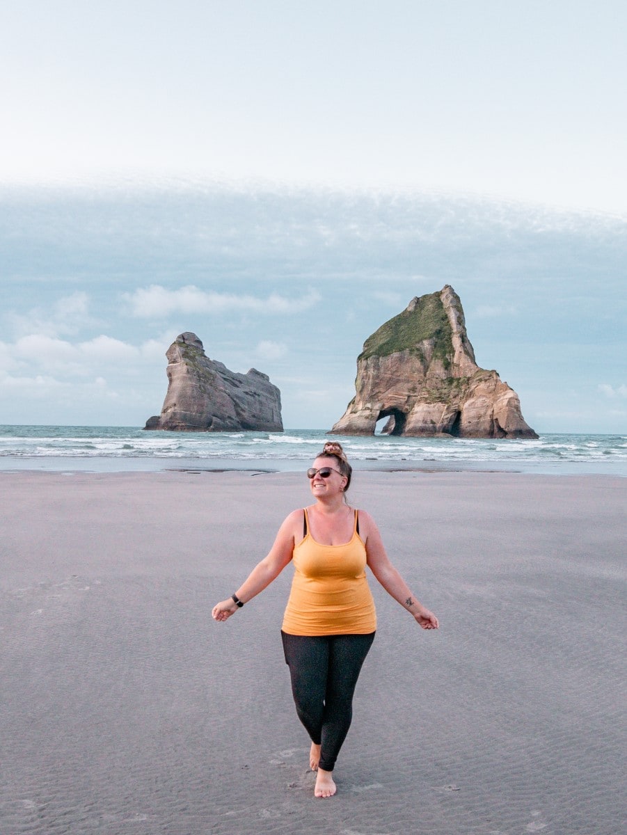 Sabrina steht am Strand mit zwei Felsfomationen im Hintergrund