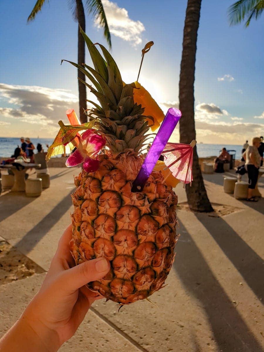 Ananas mit Strohhalm wird in der Hand gehalten und das Meer ist im Hintergrund